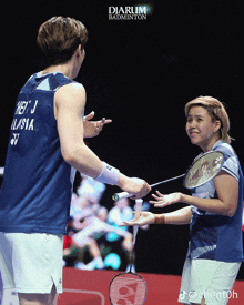 a man and a woman holding badminton rackets in front of a diarum badminton ad