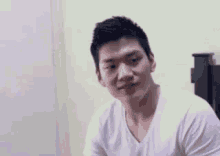 a man in a white shirt is sitting in front of a bed and smiling .