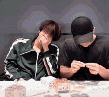two men are sitting at a table and one is covering his face