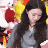 a woman stands in front of a pile of stuffed animals including a white teddy bear with a heart on it