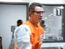 a man wearing safety goggles and an orange vest stands in front of a window with the number 1 on it