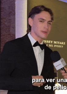 a man in a tuxedo is holding a microphone in front of a wall that says issey miyake