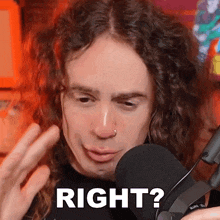 a man with curly hair is standing in front of a microphone with the words right ? written on his face .