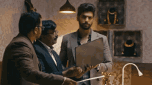 a man in a suit holds a laptop while talking to two other men