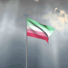 a green white and red flag is waving in the wind against a cloudy sky