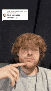 a man with curly hair and a beard is looking at the camera with his finger on his face