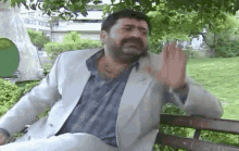 a man with a beard is sitting on a park bench making a funny face .