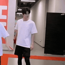 a young man wearing a white t-shirt and black shorts is standing in a hallway .