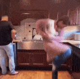 a man in a pink shirt is dancing in a kitchen with a man in a black shirt standing behind him