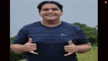 a man in a blue nike shirt is smiling and giving a thumbs up .