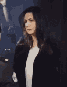 a woman in a black jacket and white shirt is standing in front of a wall .