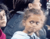 a little girl is making a funny face while sitting in a crowd .