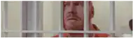 a man is behind bars in a jail cell looking out the window .