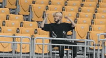 a man in a black shirt is sitting in a stadium with yellow seats with hearts on them