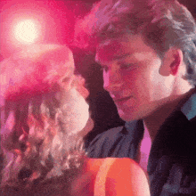 a man and a woman are dancing together in a dark room with pink lights behind them .