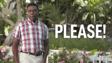 a man in a plaid shirt is standing in front of flowers and a sign that says `` please '' .
