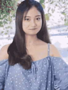 a young woman wearing a blue polka dot off the shoulder top is making a funny face .
