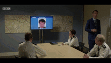 a group of police officers sit around a table in front of a bbc tv screen