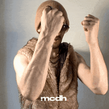 a man is wearing a fur vest and a beanie and the word mcdh is on the bottom right