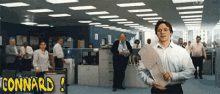a man holding a piece of paper in an office with connard written on the bottom right