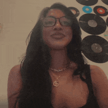a woman wearing glasses and a necklace smiles in front of a wall with records on it
