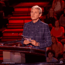 ellen degeneres is standing at a podium holding a piece of paper with game of games written on it