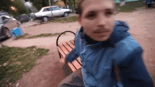 a man in a blue jacket is sitting on a bench looking at the camera .