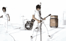 a group of people are playing instruments and singing into a microphone while standing in front of a drum set .