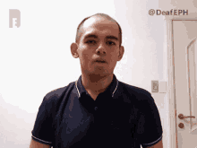 a man in a blue shirt is standing in front of a white wall with the hashtag @deafeph on it