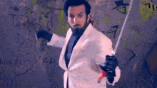 a man in a white suit holding a sword in front of a wall with graffiti on it