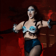 a woman in a blue bra with eyes painted on it is singing into a microphone