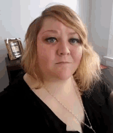 a woman wearing a black shirt and a necklace with a picture frame in the background