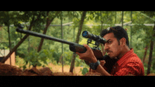 a man in a red shirt holds a rifle with a scope on it