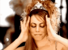 a woman is wearing a tiara on her head and covering her ears .