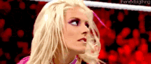a blonde woman is standing in a wrestling ring with a red background .