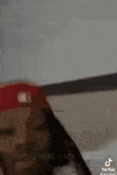 a man wearing a red hat and dreadlocks is standing in front of a white wall .