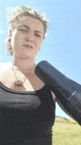 a woman in a black tank top holds a black hair dryer over her shoulder