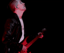 a man in a leather jacket is playing a guitar on stage in the dark .