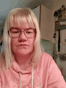 a woman wearing glasses and a pink hoodie is looking at the camera