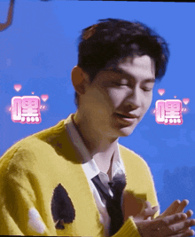 a man wearing a yellow sweater and tie is clapping his hands with a blue background