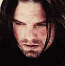 a man with long black hair and a beard is looking at the camera .