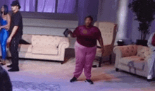 a woman in pink pants is dancing in a living room while a man watches .