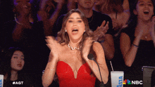 a woman in a red dress applauds in front of a crowd with a nbc logo on the bottom