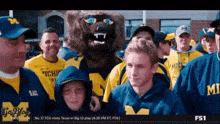 a group of people wearing michigan sweatshirts are standing in front of a mascot