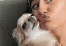 a woman is kissing a small dog on the face .
