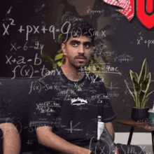 a man is sitting in front of a chalkboard with mathematical equations on it