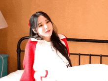 a woman is sitting on a bed wearing a red sweater