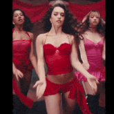 a woman in a red top and shorts is dancing with two other women in pink lingerie .