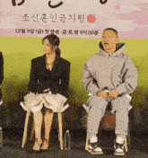 a man and a woman are sitting in front of a sign that says ' 12 ' on it