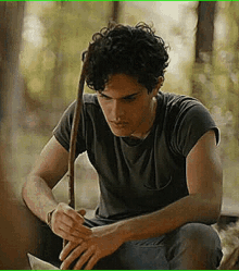 a young man is sitting in the woods with a stick in his hand